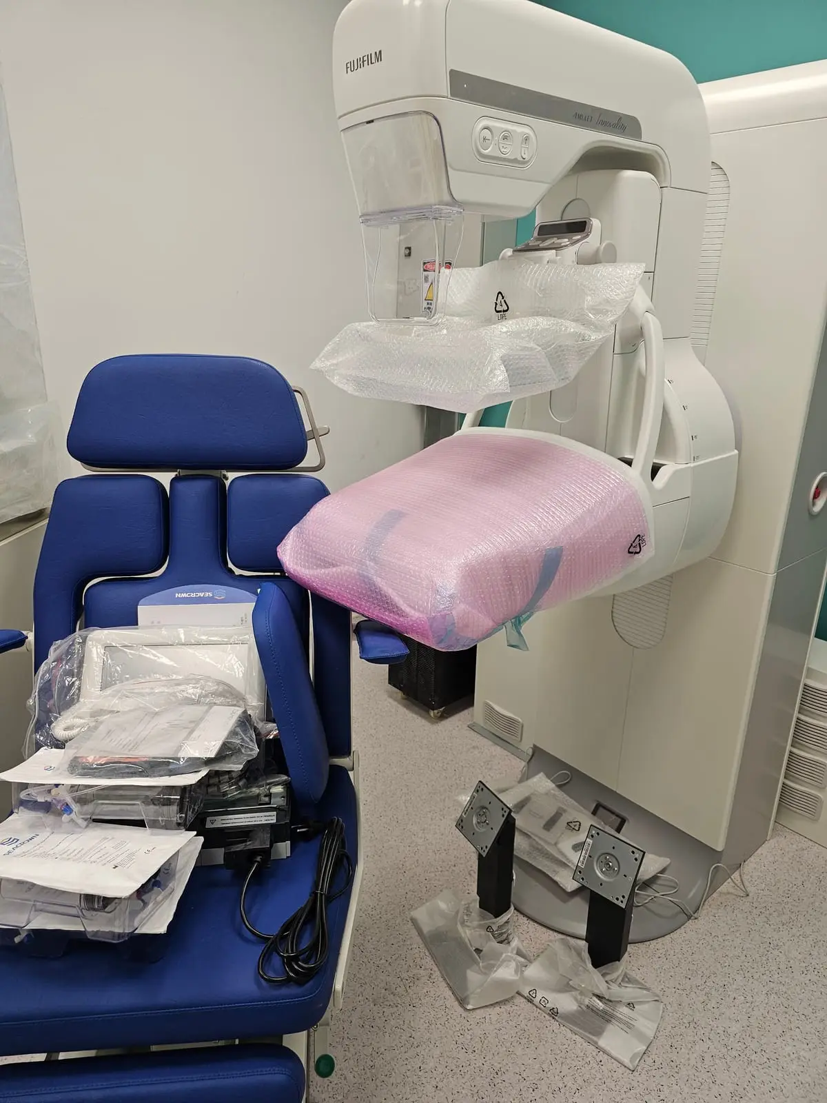 Appareil de mammographie encore sous emballage, à côté d’un fauteuil d’examen, dans une salle en cours d’aménagement.