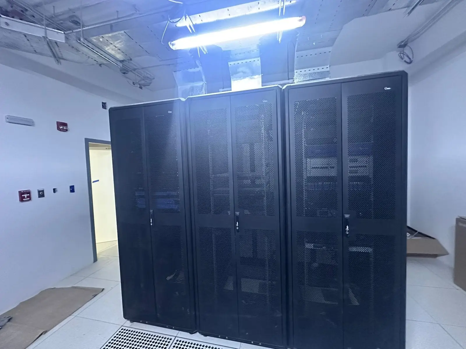 Trois baies informatiques noires alignées dans une salle technique éclairée.